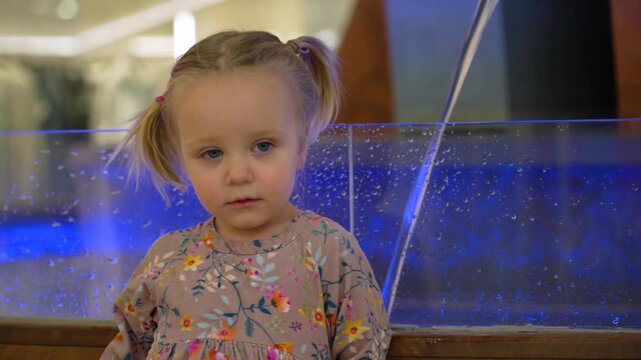 Curious young child gazes intently at captivating blue illuminated display with tiny droplets adorning glass barrier, prompting wonder and observation.
