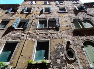 Old weathered building facade in Venice with peeling paint and open shutters