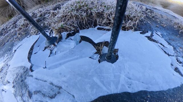 Trekking poles breaking a frozen puddle in the mountains
