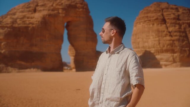 Man traveling in Saudi Arabia, standing beside Elephant Rock in AlUla. Trip in the Arabic desert. Sightseeing in Arab country, in Al Ula location