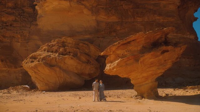 Couple travels in Saudi Arabia, man and woman stand by sand rocks in AlUla. Tourist destination in Al Ula desert