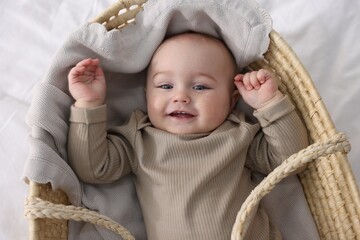 Cute little baby in wicker basket on bed, top view