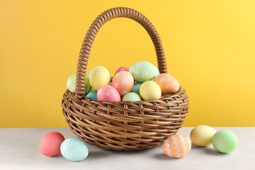 Fototapeta premium Beautiful Easter eggs in basket on white table against yellow background