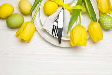 Easter celebration. Festive table setting with tulip flowers and painted eggs on white wooden...