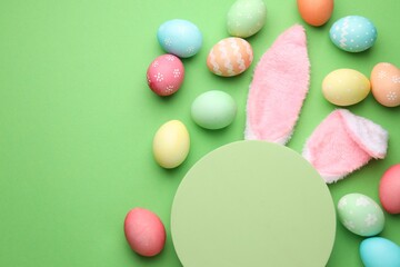 Happy Easter. Cute bunny ears, empty podium and painted eggs on green background, flat lay. Space for text