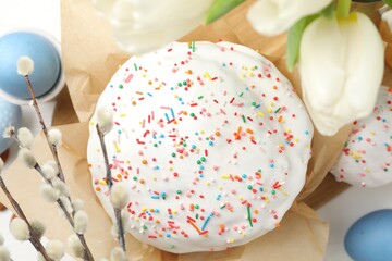 Tasty Easter cakes, painted eggs, willow branches and tulips on white wooden table, flat lay