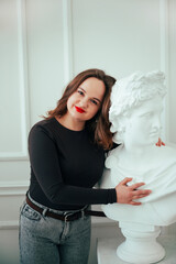 Naklejka premium Woman poses with a white bust statue in a bright indoor setting during the day