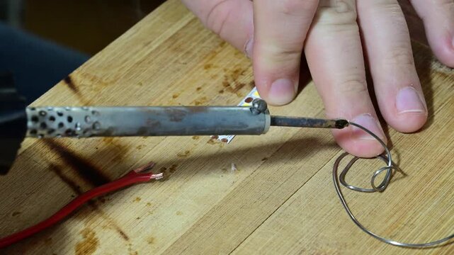 hands using a hot soldering iron to carefully apply solder to the copper contacts of an LED strip on a wooden workbench.