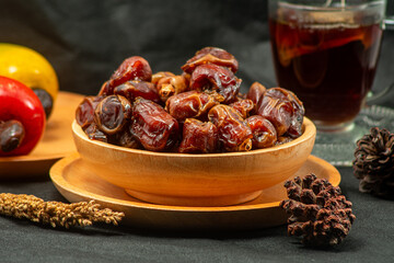 Close-up of premium dried dates piled in a wooden bowl with a blurred tea cup background.