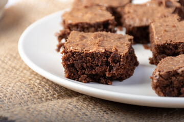 Close-up of a chocolate brownie cut into pieces on a white plate.