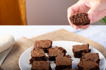 Hand taking a piece of chocolate brownie from a white plate.