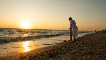 Brother and sister interacting with the calm waves along the sandy shore during a beautiful golden hour sunset, showing a carefree family moment on vacation.