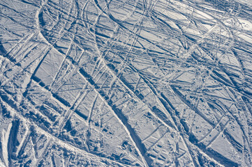 Obraz premium Aerial top view of messy ski and snowboard tracks on a white snow slope. Abstract winter texture of mountain resort trail, active lifestyle and sports background