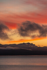 orange sunset on the shores of the lake with mountains in the background