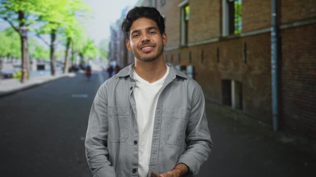 Man holding chocolate bar in right hand and shrugging with left palm up on street beside a brick building; contentment indulgence.