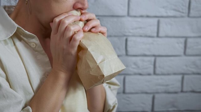 Stressed woman breathing into paper bag during panic attack. Woman experiencing a panic attack, breathing heavily into a brown paper bag to regulate her breathing and calm down her anxiety