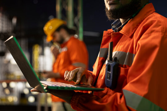 Close up of specialist on drilling rig deck managing operational workflows using laptop late at night. Offshore platform expert documenting machinery hazard reports after finishing safety inspection