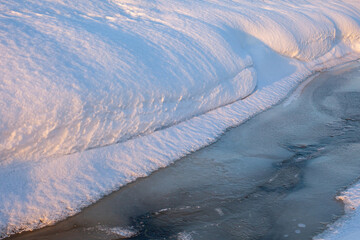 Abstract winter scene with frozen stream and smooth snowdrifts. Soft light highlights snow texture and icy water, creating a calm, minimalist winter background