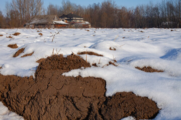 Melting snow on agricultural field revealing soil beneath. Rural landscape during winter thaw, symbol of climate change, seasonal transition and environmental processes in farmland