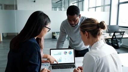A diverse team of analysts collaborates on a complex data problem, pointing at charts on a laptop in a modern office - Powered by Adobe