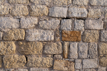 Detailed texture of a weathered stone wall made of rough limestone blocks. The surface shows natural erosion, cracks, and warm tones, ideal for architectural, historical, or design backgrounds.