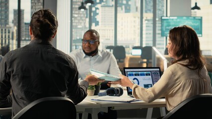 Business people greeting each other in office before a briefing meeting, colleagues discuss budgeting and project development. Diverse work team reviews reports and data on laptop.