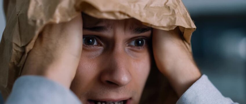 A visibly distressed man reacts to overwhelming emotional pressure with a paper bag.