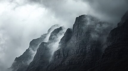 Misty mountain peaks shrouded in dense fog above rugged rocky cliffs, a dramatic and moody natural landscape