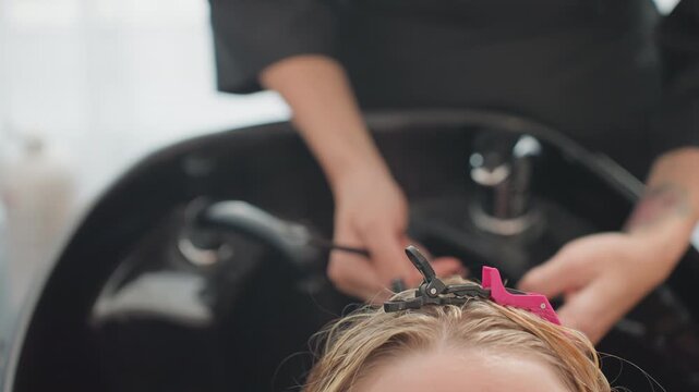 Salon shampoo bowl hair wash, tattooed stylist gently lathers clients scalp over black basin, pink clip securing hair, creamy suds and warm rinse, reclining client enjoying professional care and calm