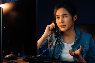 Young beautiful Asian creative woman calling on phone desk to customer or coworker explaining creator project's high profit while searching market analysis on pc at neon office at night. Stratagem.