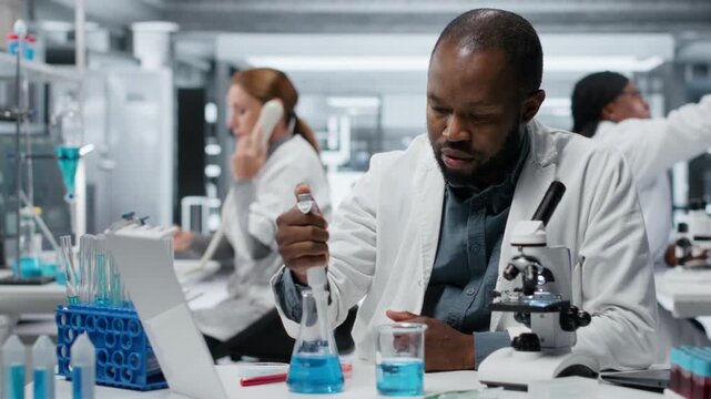 Analytical chemist pipetting blue liquid into test tube to analyze it. African american man transferring chemical sample in glass flask to prepare for spectroscopic analysis, camera B