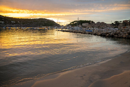 Golden sunset illuminates Port de Soller Majorca harbor, boats, and coastal town