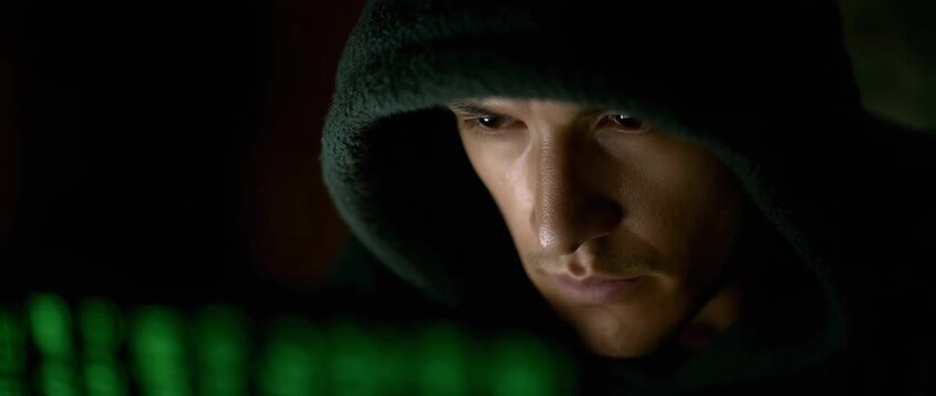 A concentrated man works on a computer in dim lighting.