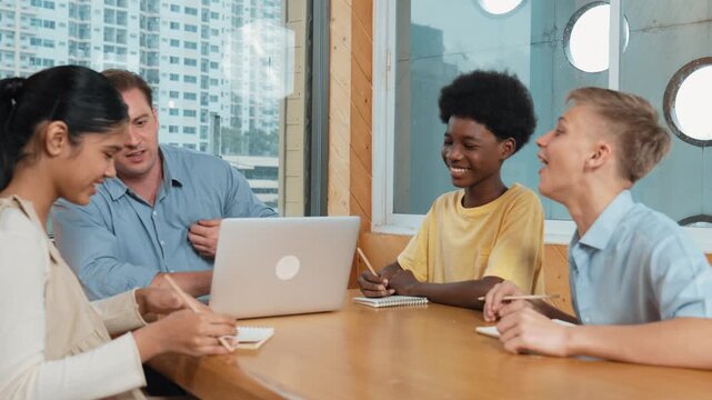 Smart girl ask teacher a question while show idea while diverse student working classwork. Group of multicultural children pointing at notebook while happy boy sharing idea at classroom. Edification