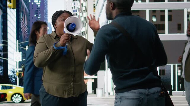 Black woman amplifying voice with a loudspeaker promoting business, commercial selling on the street with pedestrians walking during commute. Dynamic urban everyday city life. Camera A.