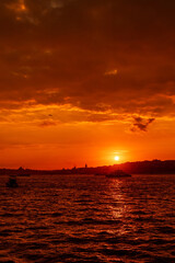 Fototapeta premium Beautiful red sunset over the Bosphorus with dramatic burning sky, shimmering water and boats, looking toward Beyoglu and Eminonu on European side of Istanbul, Turkey