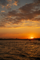 Fototapeta premium Beautiful glowing sunset on the European side of Istanbul, Turkey from Bosphorus toward Karakoy and Eminonu, with the silhouettes of Galata Tower and Suleymaniye Mosque against burning sky