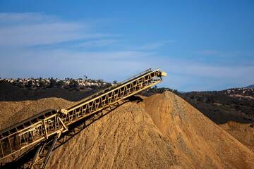 A conveyor machine and a large mound of dirt and gravel at a construction site