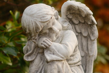 Naklejka premium Close-up of weathered angel statue in a garden, stone sculpture with wings