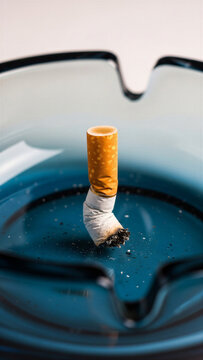 Extinguished cigarette butt in blue glass ashtray focused on smoking habits