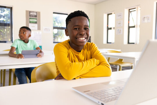 African American child boys sitting in classroom front smiling at silver laptop rear holding tablet