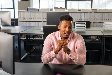 African American man sitting and speaking at desk in open-plan office with monitor and binders © wavebreak3
