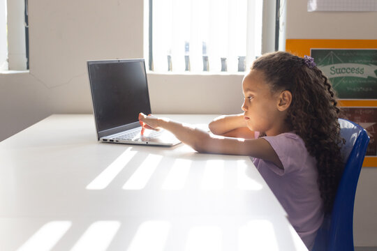 African girl child sitting at table reaching for laptop by blinds with Success poster, copy space