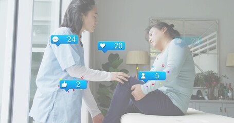 Leaning Korean woman in light-blue scrubs checking man holding knee during home visit, social icons
