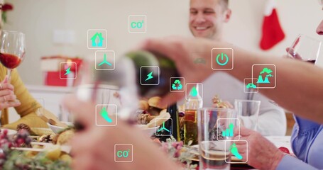 Pouring family member wearing white shirt serving wine at holiday dinner at home, with green icons