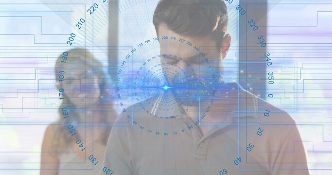 Standing man in polo studying blue HUD in office, partner in sleeveless top and glasses observing - Powered by Adobe