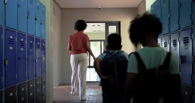 African American woman entering walking past lockers guiding children carrying packs into classroom