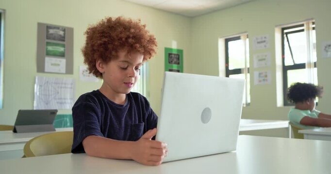 Classroom child, African American boy placing white laptop, typing task in class as teacher passes
