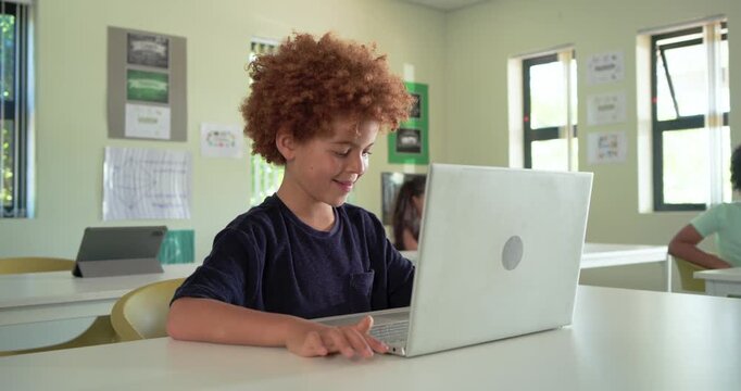 African American boy child typing, glancing, smiling on silver laptop in class while camera nearing