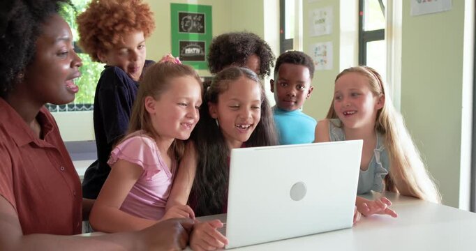 Diverse students, African American teacher in rust blouse pointing at laptop, watching and laughing